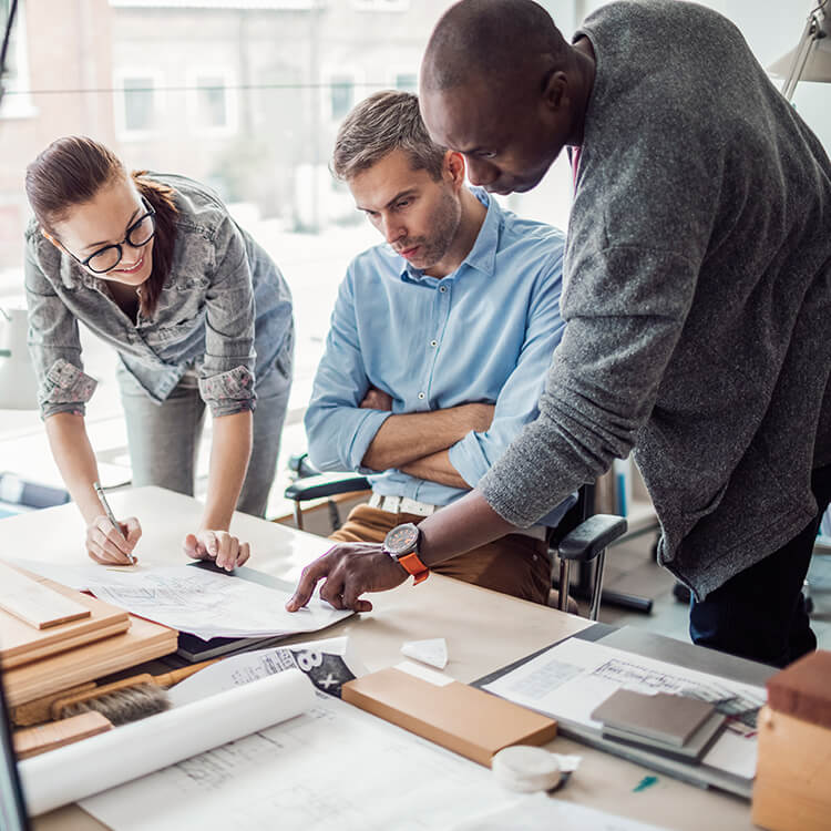 Two men and a woman positioned around a desk viewing plans to grow their environmental and engineering firm.